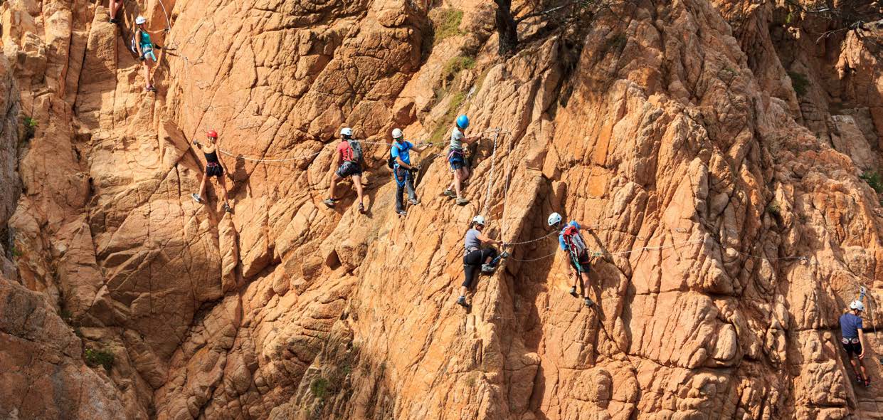 Helmeted climbers following a fixed-cable route across a rock face